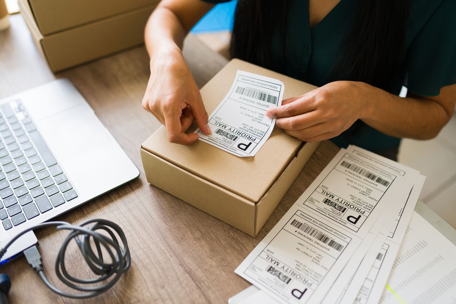 Closeup of a female business owner preparing a shipment, affixing a priority mail label to a cardboard box at her small business office